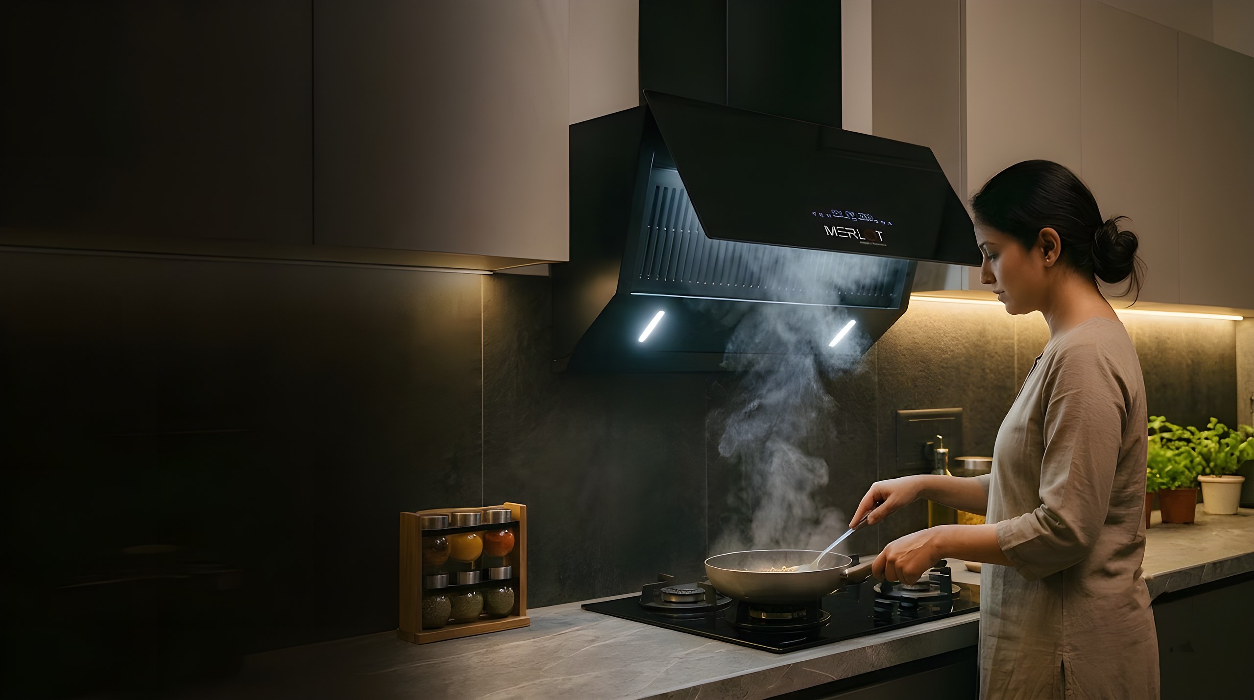 Woman cooking beneath a Merlot BLDC auto-open chimney from the Kyra and Myra series, drawing in the smoke